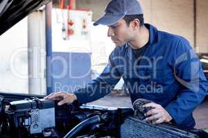Might need a new battery. a handsome young male mechanic working on the engine of a car during a service.