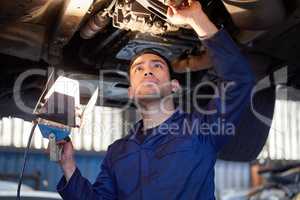 Taking a closer look. a handsome young male mechanic working on the engine of a car during a service.