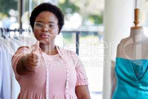 You need it, weve got it. an attractive young seamstress giving thumbs up while working in her boutique.