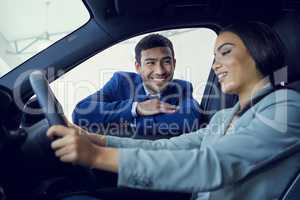 So, what do you think. an attractive young woman sitting in a new car while speaking to a handsome male car salesman about a deal.