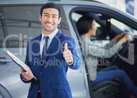 Looks like Ive made the sale. Cropped portrait of a handsome young male car salesman giving thumbs up on the showroom floor with a female customer in a vehicle behind him.