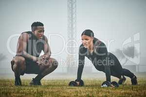 This is your last rep, give it your all. a sporty young woman exercising with dumbbells with the help of a trainer outdoors.