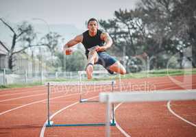 No obstacle too big. Full length shot of a handsome young male athlete practicing hurdles on an outdoor track.