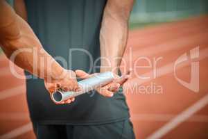 Its up to you now. Rearview shot of an unrecognizable male athlete grabbing a baton from his teammate during a relay race.