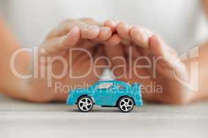 Take care of your car. a unrecognizable female covering a toy car with his hands at home.