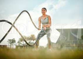 Pure power. Full length shot of an attractive young female athlete exercising with battle ropes outside.