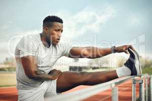 Limbering up those legs. a handsome young male athlete warming up before starting his outdoor workout.