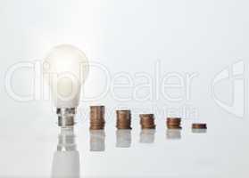 It pays to be resourceful with your money. Studio shot of a lightbulb alongside a stack of coins against a white background.