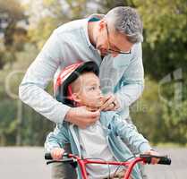 Dad says that I should always be safe. a little boy sitting on his bicycle while his dad ties his helmet.