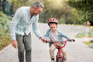 Its his bike ride. a little boy wearing a helmet and riding a bike outside with his father.