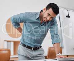 Hes starting to feel the strain of sitting too long. a young businessman experiencing back pain while working in an office.