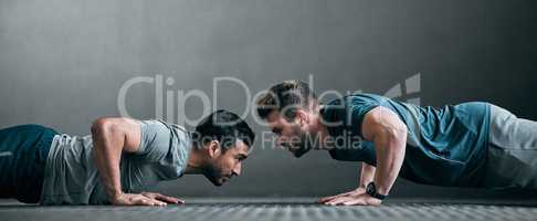 Game on. Full length shot of two handsome young male athletes doing pushups face to face against a grey background.