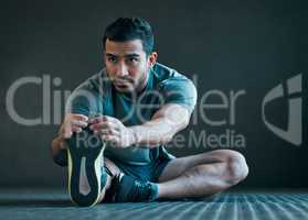 Stay limber. Full length shot of a handsome young male athlete warming up against a grey background.