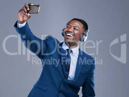 Smile Its selfie time. Studio shot of a handsome young businessman using his cellphone to take selfies while listening to music on headphones against a grey background.