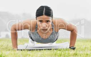 Feel the burn. Full length portrait of an attractive young female athlete doing pushups while exercising outside.