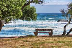 Relaxing bench with sea or ocean view to enjoy calm, peaceful or zen beach with waves washing on shore in remote area. Scenic seating, blue sky and copy space in a coastal park on the promenade