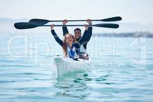 Theyre always up for trying something new. Portrait of a young couple raising their oars while kayaking together at a lake.