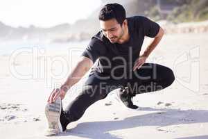 The warmup is part of the workout. Full length shot of a handsome young male athlete warming up before his workout on the beach.