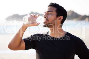 Keep your cool while working out. a handsome young male athlete hydrating during his workout on the beach.