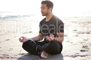Its a matter of balance. Full length shot of a handsome young male athlete meditating on the beach.