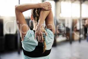 Dont forget to stretch. Rearview shot of a young woman stretching at the gym.