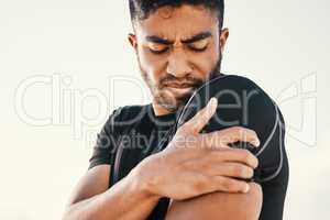 No more exercise for me. a handsome young male athlete holding his shoulder in pain while exercising on the beach.