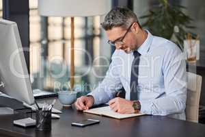 Detailed days makes for smooth sailing. a mature businessman writing in a notebook while sitting at a desk in a modern office.