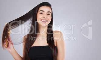 Brush for shine and health. Studio portrait of an attractive young woman brushing her hair against a grey background.
