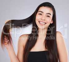 Smooth your hair while keeping it nourished. Studio portrait of an attractive young woman brushing her hair against a grey background.