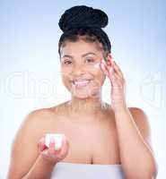 A gorgeous glow to combat harsh weather. Studio portrait of an attractive young woman applying moisturiser to her face against a blue background.