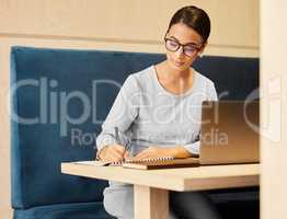 Drawing up a list of potential customers. an attractive mature businesswoman taking notes while working on her laptop at a desk in the office.