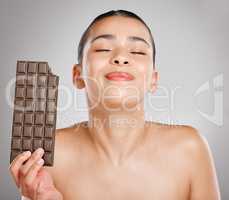 Having chocolate is like a hug on the inside. Studio shot of an attractive young woman eating a slab of chocolate against a grey background.