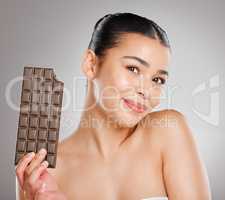 Is there anything sweeter than chocolate Yes, me. Studio shot of an attractive young woman eating a slab of chocolate against a grey background.