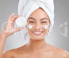 Skin care must be good enough to eat. an attractive young woman applying moisturiser to her face against a studio background.