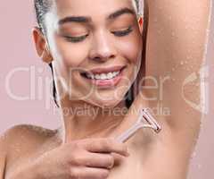 Smooth skin for the win. a young woman shaving her armpits against a studio background.