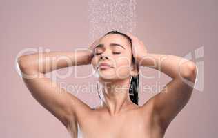 A haircare routine is essential. a young woman rinsing her hair against a studio background.