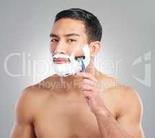 The fine art of sculpting facial hair. Studio shot of a handsome young man shaving against a grey background.