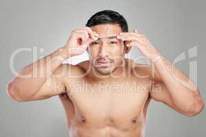 A good day starts with well defined eyebrows. Studio shot of a handsome young man plucking his eyebrows against a grey background.