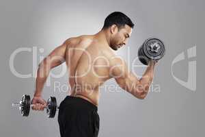 Look out Im throwing it. Studio shot of a young man practicing his bicep curls against a grey background.