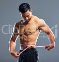 Take care of your physique. Studio shot of a muscular young man measuring his waist against a grey background.