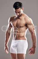 Showing off his rock hard abs. Studio shot of a muscular young man posing against a grey background.