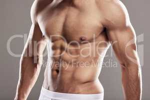 Touch them, theyre real. Studio shot of a muscular young man posing against a grey background.