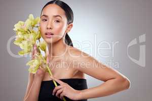 Embrace the natural beauty within you. Studio portrait of a beautiful young woman posing with orchids against a grey background.