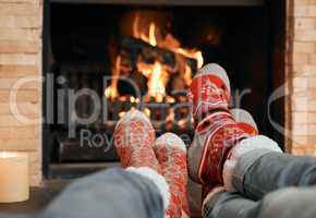 Cosying up around the fireplace. Closeup shot of a couple wearing Christmas socks while relaxing with their feet up by a fireplace at home.