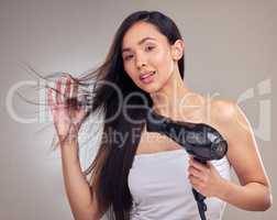 Life would be dull with boring hair. an attractive young woman standing alone and using a hairdryer in the studio.
