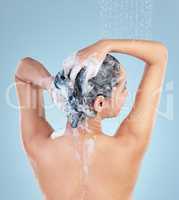 The best shampoo in the haircare business. Rearview studio shot of an attractive young woman washing her hair while taking a shower against a blue background.