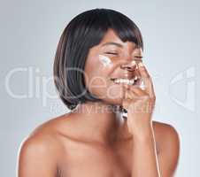 Just a dab does a lot. Studio shot of an attractive young woman applying moisturiser to her face against a grey background.