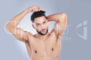 Tame hair, wild heart. Studio shot of a handsome young man combing his hair against a grey background.