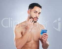 A must have for my morning shave. Studio shot of a handsome young man applying cologne against a grey background.