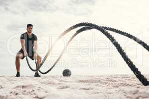 Im stronger than the voice telling me to quit. a sporty young man exercising outside with heavy ropes.